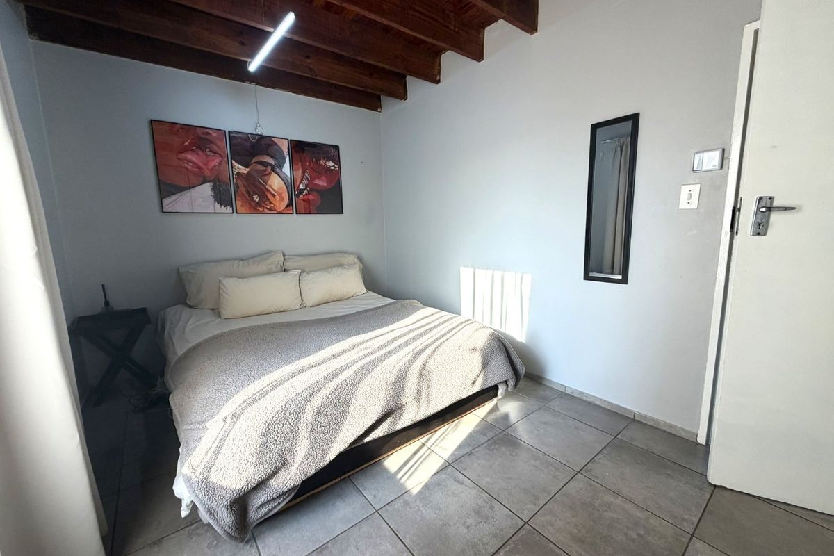 A bedroom featuring exposed timber ceiling beams and tiled flooring, providing a rustic aesthetic with neutral wall finishes.