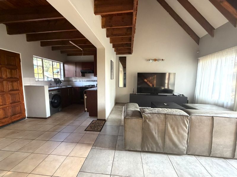 Open-plan living area featuring vaulted ceilings with exposed timber beams, tiled flooring, and an integrated kitchen space.