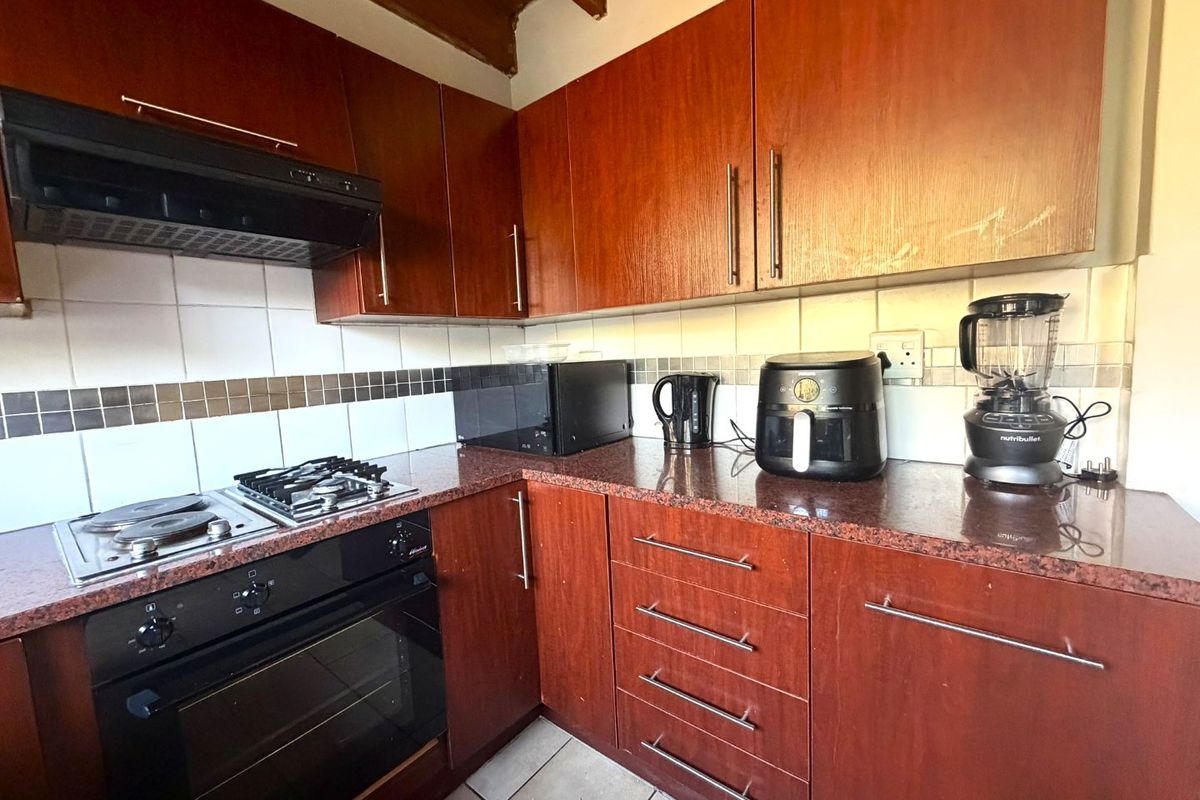 A functional kitchen featuring dark wood cabinetry, granite countertops, a combination gas and electric hob, built-in oven, and a tiled backsplash.