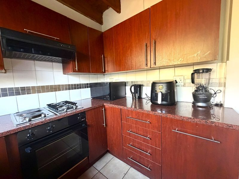 A functional kitchen featuring dark wood cabinetry, granite countertops, a combination gas and electric hob, built-in oven, and a tiled backsplash.