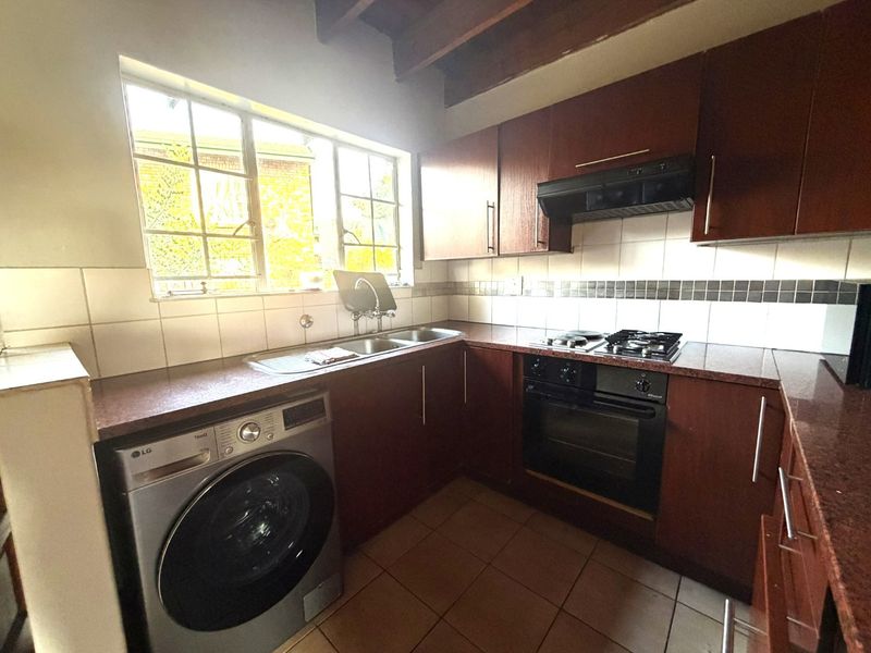 A functional kitchen featuring dark wood cabinetry, tiled splashbacks, built-in oven with gas hob, and exposed timber ceiling beams.