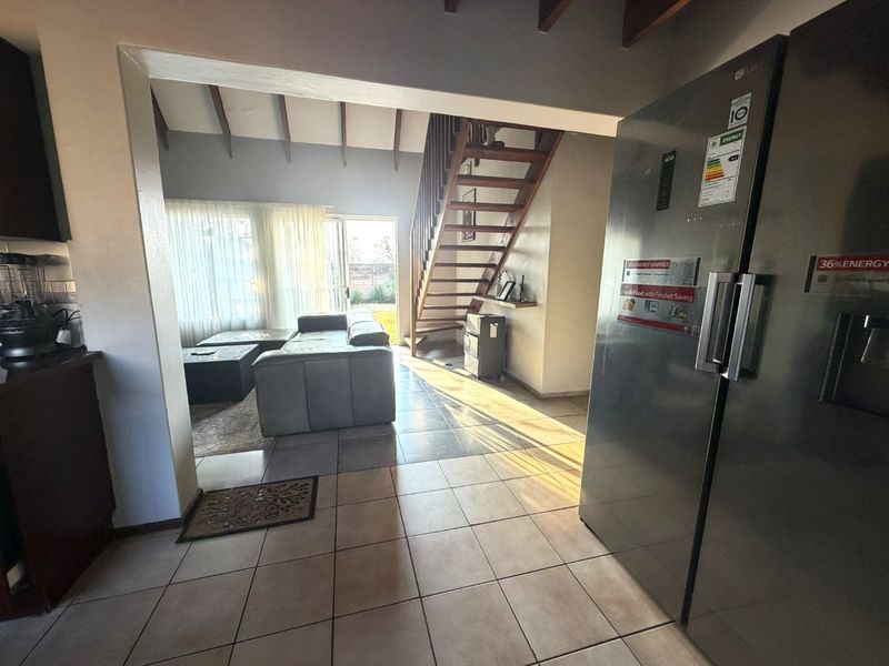 Open plan living area featuring tiled flooring, exposed timber ceiling beams, and a timber staircase leading to the upper level.