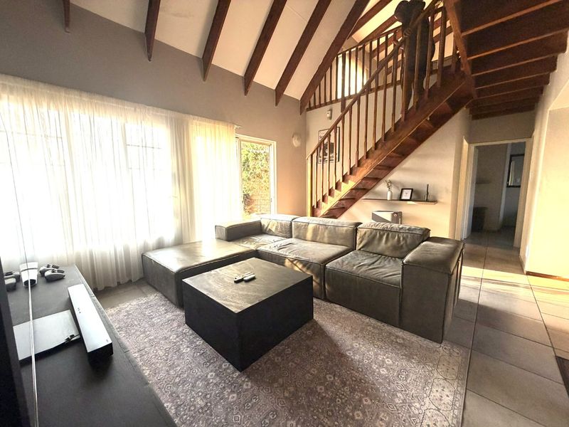 Spacious living room featuring high vaulted ceilings with exposed timber rafters, a prominent timber staircase, and tiled flooring with natural light.