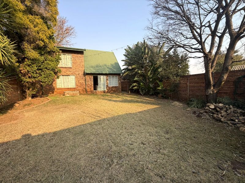 Rear view of the townhouse featuring a private garden, brick facade, and tiled roof with established trees and boundary walling.