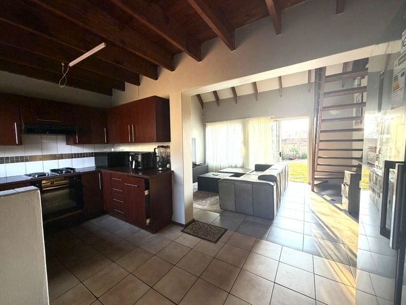 Open-plan kitchen and living area featuring dark wood cabinetry, tiled flooring, exposed timber ceiling beams, and a spiral staircase leading to the upper level.