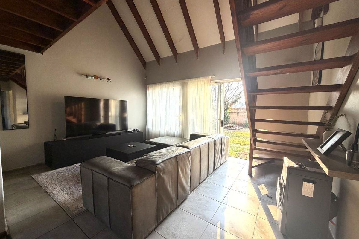 Spacious living room featuring a vaulted ceiling with exposed timber beams, tiled flooring, and a timber staircase leading to the upper level.