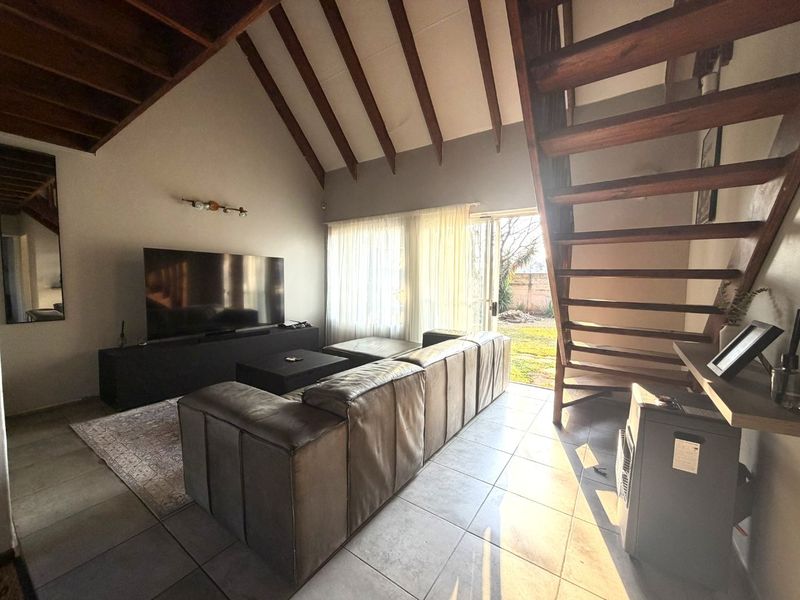 Spacious living room featuring a vaulted ceiling with exposed timber beams, tiled flooring, and a timber staircase leading to the upper level.
