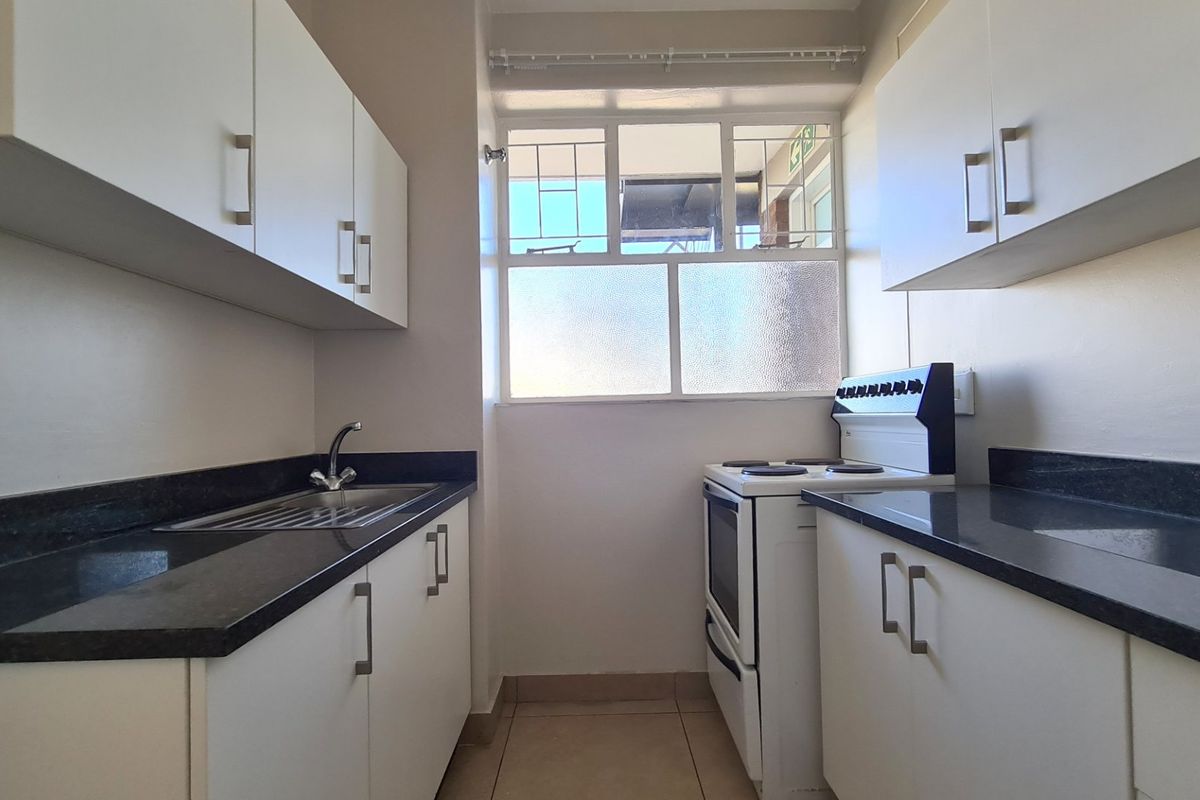 A clean, functional kitchen featuring white cabinetry, dark countertops, a stainless steel sink, and a freestanding stove with natural light from the window.