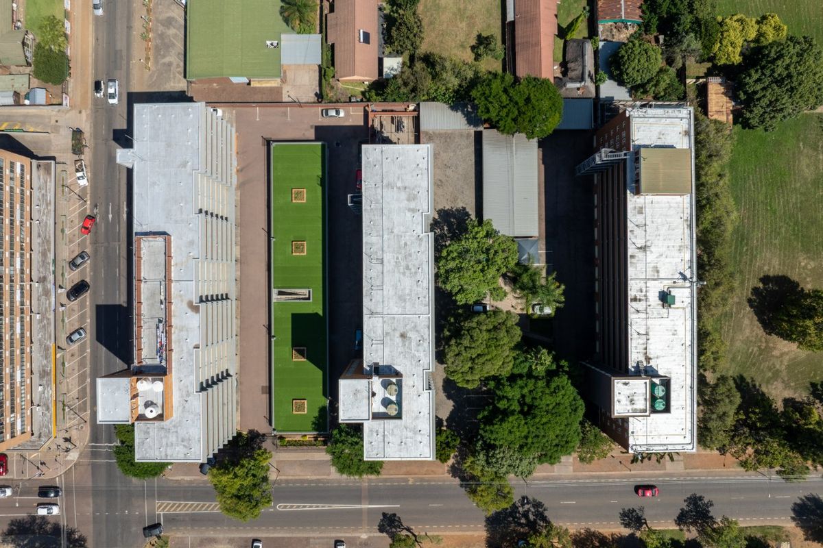 Aerial view of a commercial property complex featuring multiple buildings with flat roofs, HVAC installations, paved parking, and landscaped green spaces.