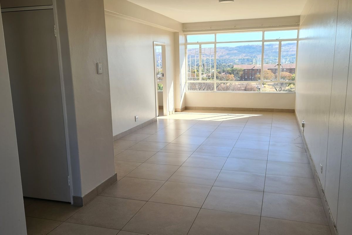 A bright, empty living area featuring large windows with scenic views and neutral tiled flooring throughout.