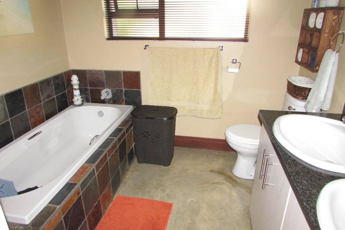 A functional bathroom featuring a built-in bathtub with slate tile surround, a dual vanity with granite countertop, and a toilet.