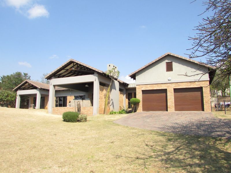 Front view of a residential house featuring a double garage, paved driveway, and a covered patio area with brick and plaster finishes.