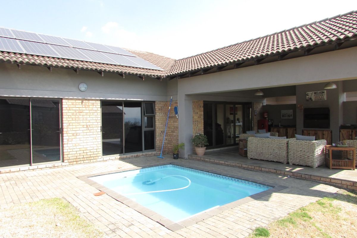 Outdoor entertainment area featuring a swimming pool, covered patio, and brick facade with roof-mounted solar panels.