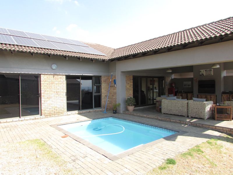 Outdoor entertainment area featuring a swimming pool, covered patio, and brick facade with roof-mounted solar panels.