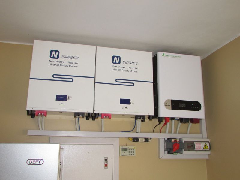 Utility area featuring a modern solar power installation with two lithium battery modules and a hybrid solar inverter.