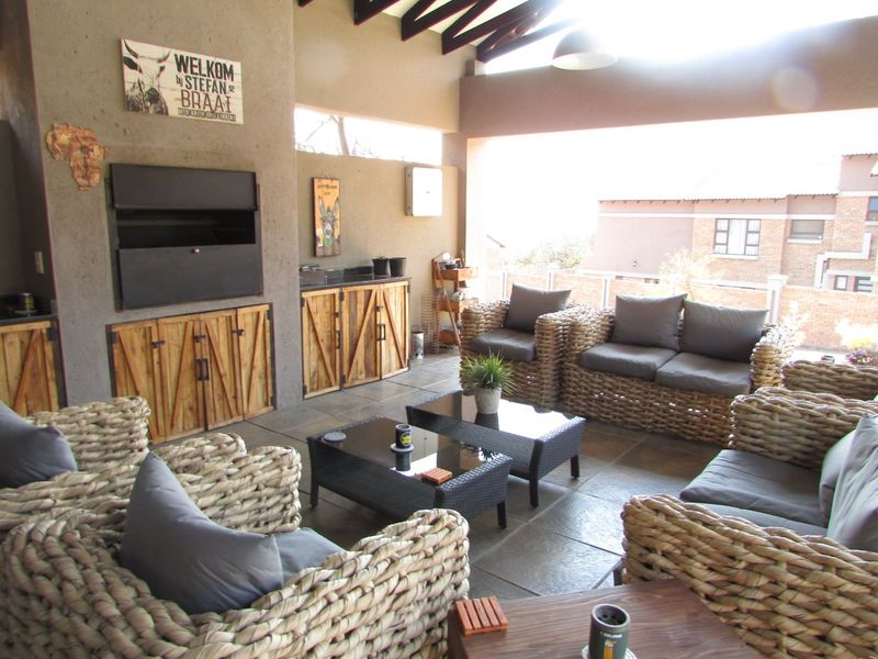 Covered patio area featuring a built-in braai, stone tile flooring, and exposed timber rafters, ideal for outdoor entertaining.