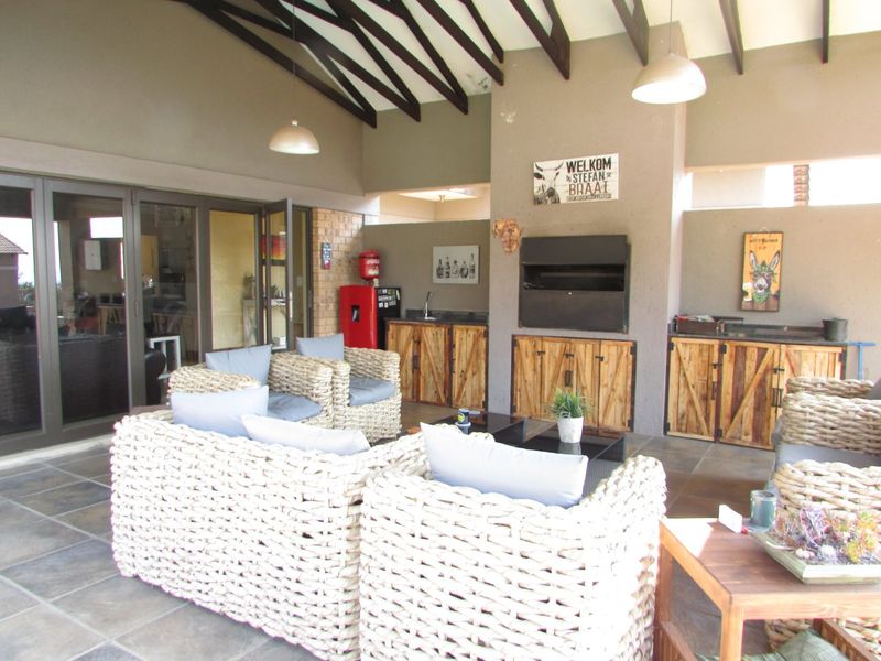 Spacious covered patio featuring exposed timber rafters, tiled flooring, built-in braai, and custom cabinetry with integrated sink, perfect for outdoor entertaining.