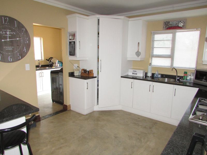 A functional kitchen featuring white cabinetry, dark granite countertops, polished concrete floors, and an adjoining scullery area with additional storage and workspace.