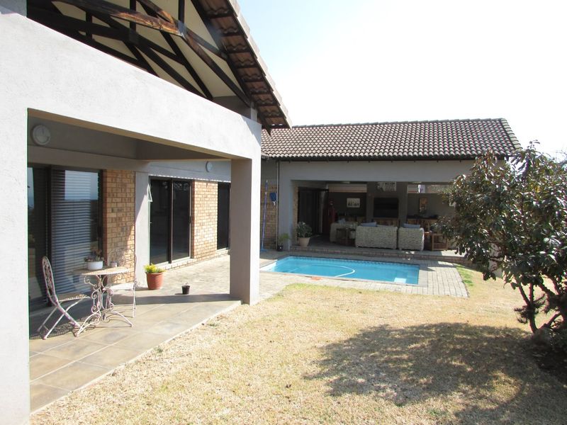Rear exterior view featuring a covered patio, a swimming pool, and a paved outdoor entertainment area with brick and plaster finishes.