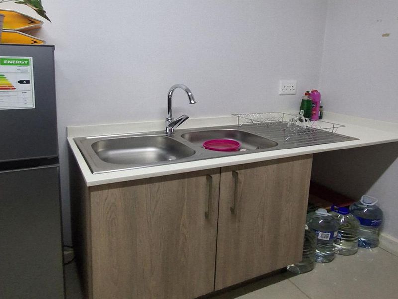 A functional scullery area featuring a stainless steel double sink, chrome mixer tap, laminate countertop, and built-in base cabinetry for storage.