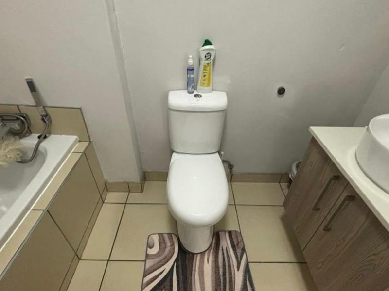 A functional bathroom featuring a built-in bathtub, a standard toilet, and a vanity cabinet with a vessel sink, finished with tiled flooring.