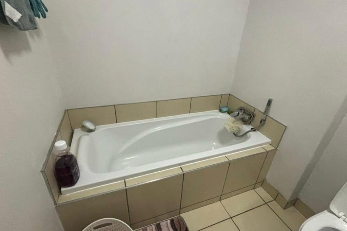 A functional bathroom featuring a built-in bathtub with tiled surround, chrome fixtures, and ceramic floor tiling.
