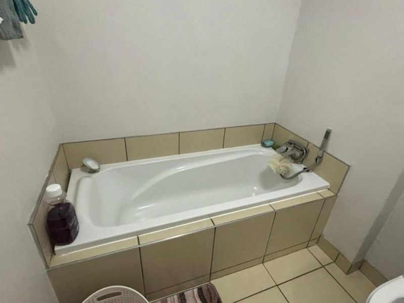 A functional bathroom featuring a built-in bathtub with tiled surround, chrome fixtures, and ceramic floor tiling.