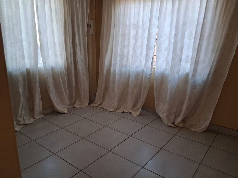 An empty living area featuring neutral tiled flooring and large windows with installed curtain tracks, offering a blank canvas for interior design.