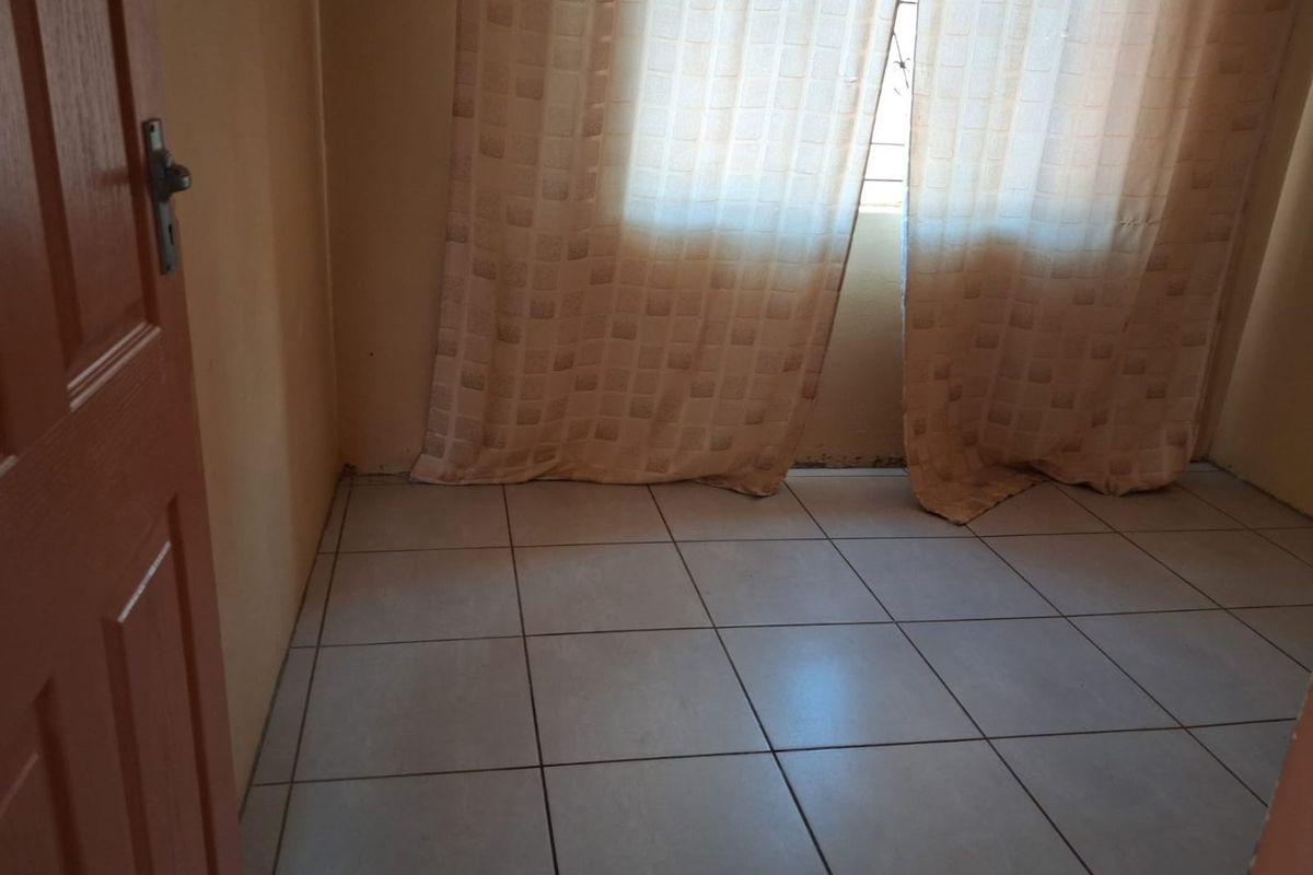 A simple, empty bedroom featuring neutral tiled flooring and a standard timber door, providing a blank canvas for potential interior design updates.