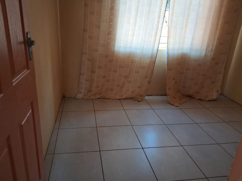 A simple, empty bedroom featuring neutral tiled flooring and a standard timber door, providing a blank canvas for potential interior design updates.