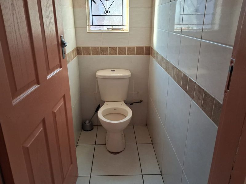A compact, tiled guest bathroom featuring a standard toilet and a small window with security bars.