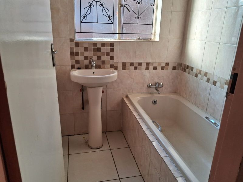 A functional bathroom featuring a pedestal basin, a built-in bathtub, and neutral tiled finishes throughout.