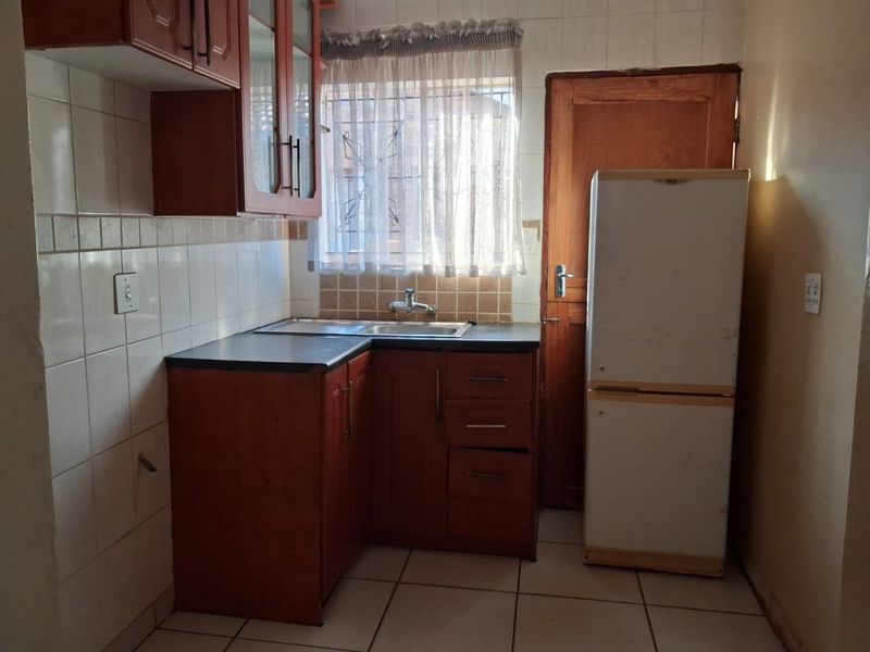 A compact kitchen featuring wooden cabinetry, tiled splashbacks, and tiled flooring, offering a functional layout with potential for modern updates.