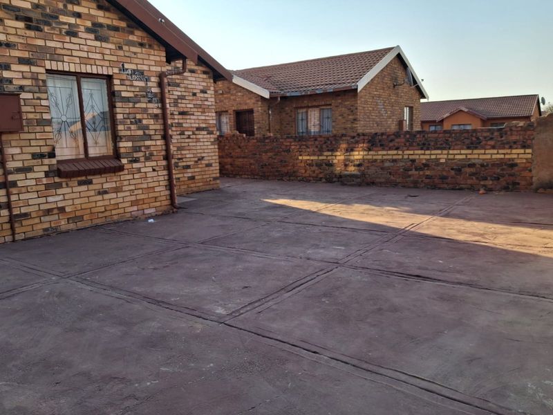 A rear exterior view of a face brick house featuring a paved courtyard area and a surrounding brick boundary wall.