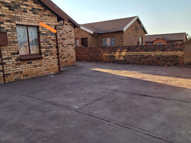 A rear exterior view of a face brick house featuring a paved courtyard area and perimeter brick walling.
