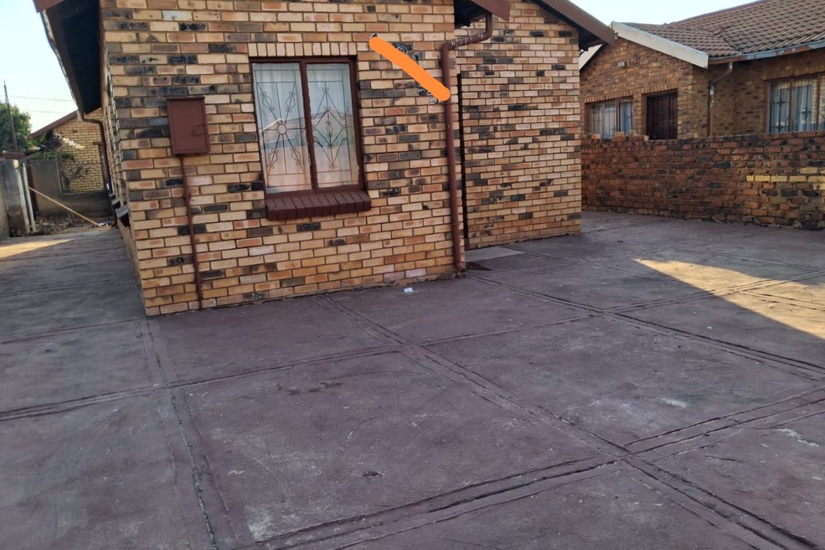 Rear exterior view of a face brick house featuring a paved courtyard area and secure window bars.