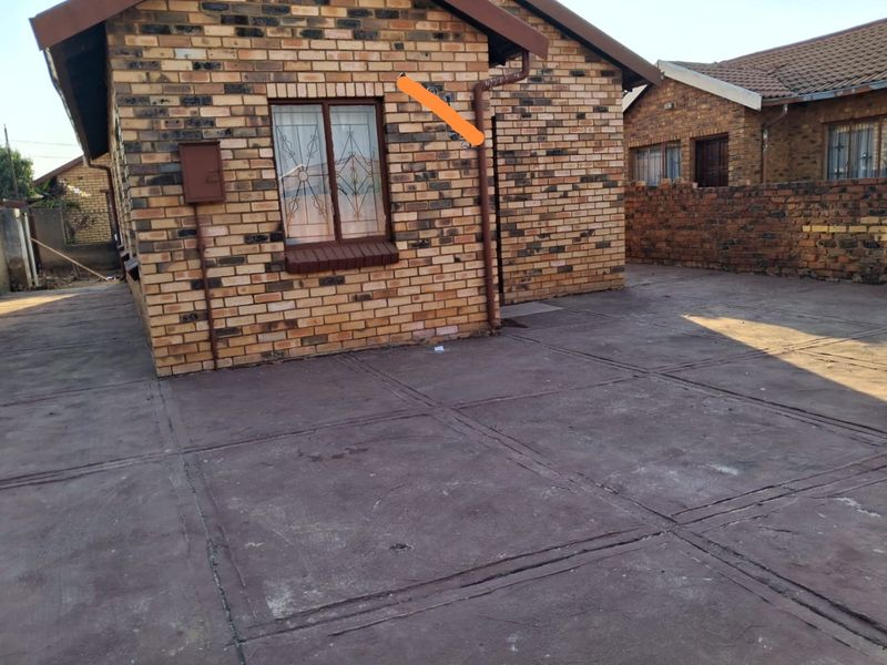 Rear exterior view of a face brick house featuring a paved courtyard area and secure window bars.