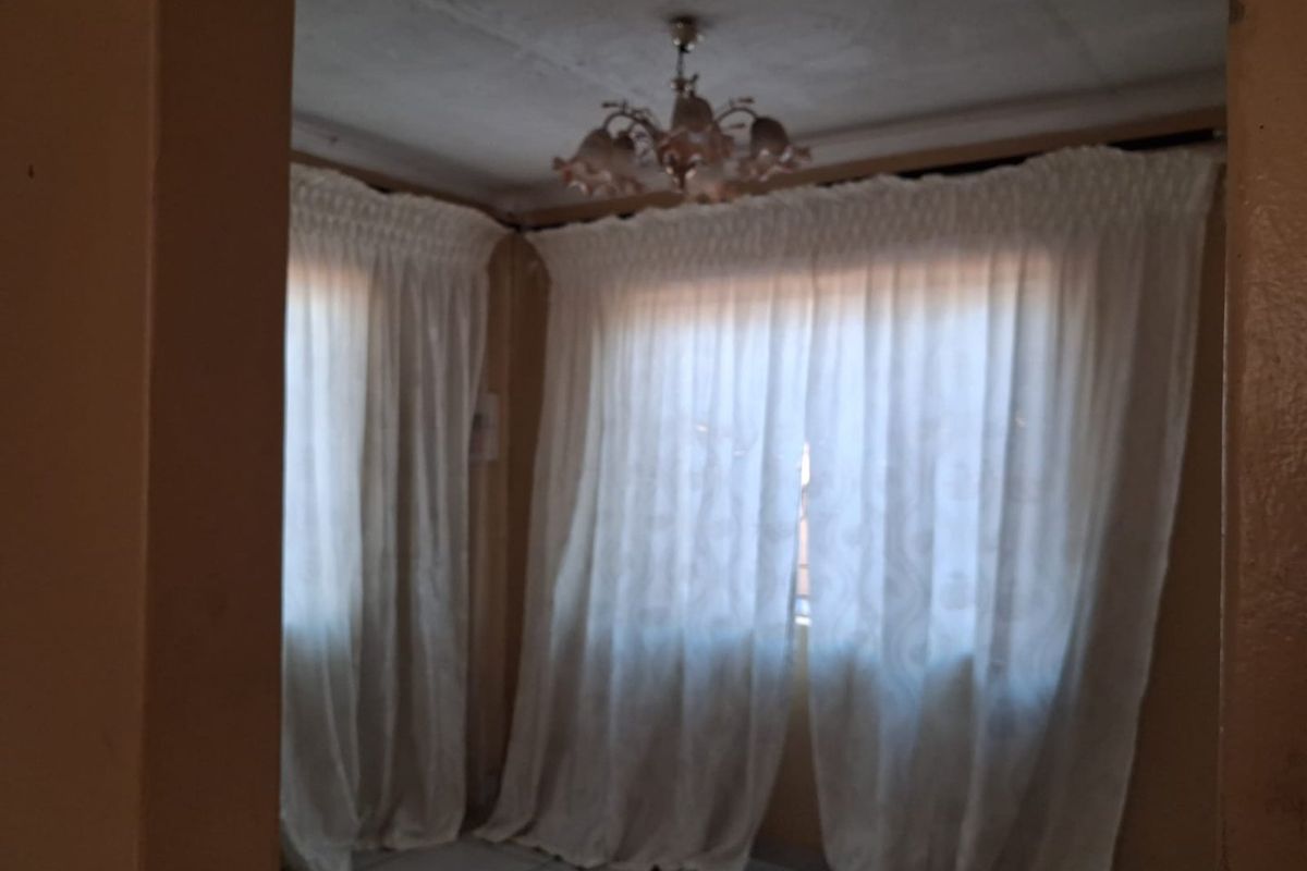 A vacant living room featuring tiled flooring and a decorative ceiling light fixture, requiring cosmetic updates to improve its overall condition.