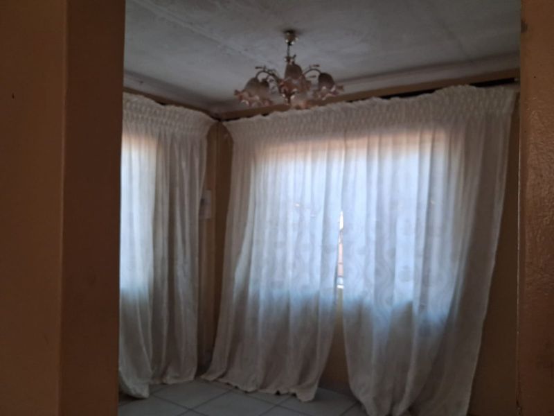 A vacant living room featuring tiled flooring and a decorative ceiling light fixture, requiring cosmetic updates to improve its overall condition.