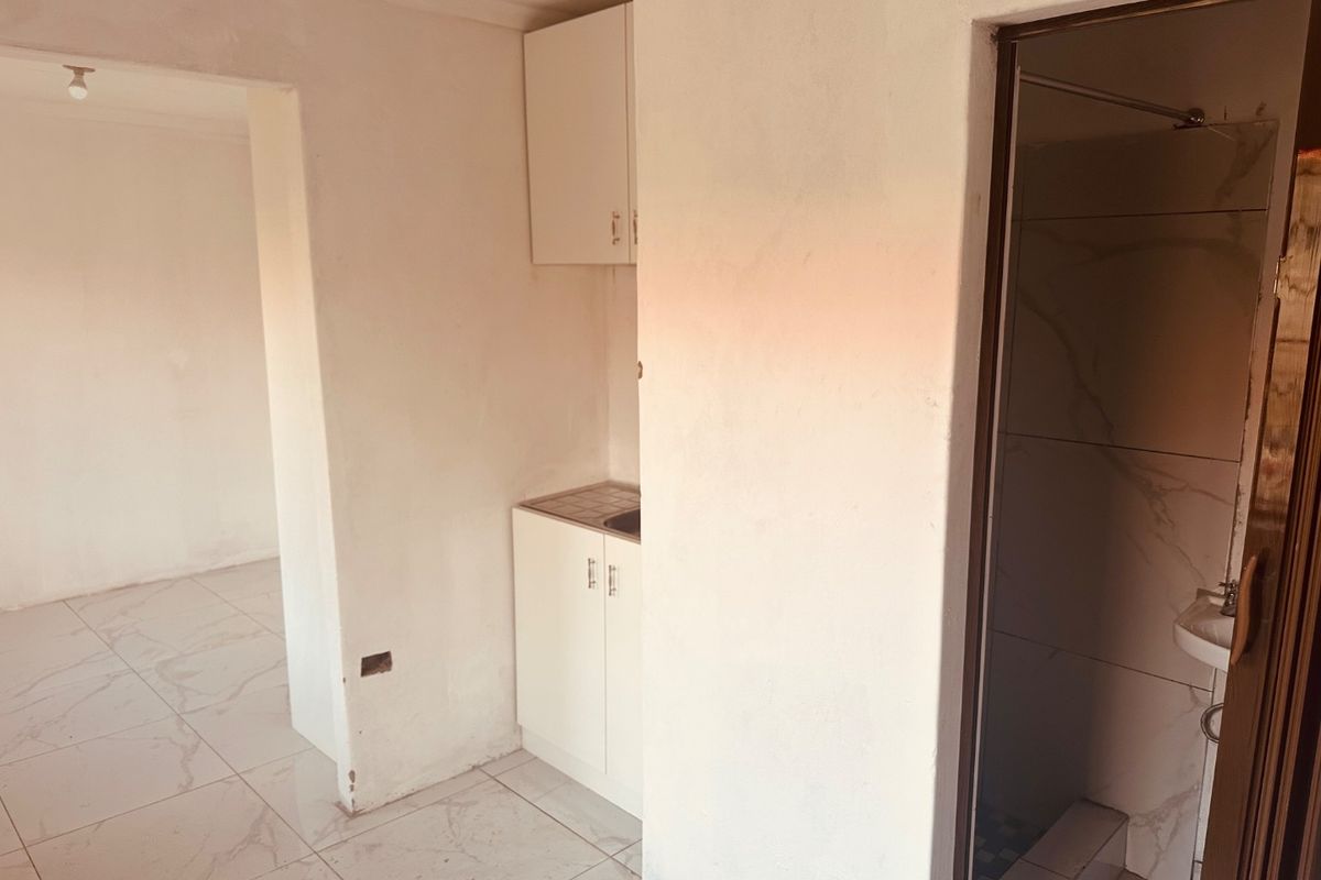 A compact kitchen area featuring built-in cabinetry and sink, adjacent to a tiled bathroom space in an unfinished apartment interior.