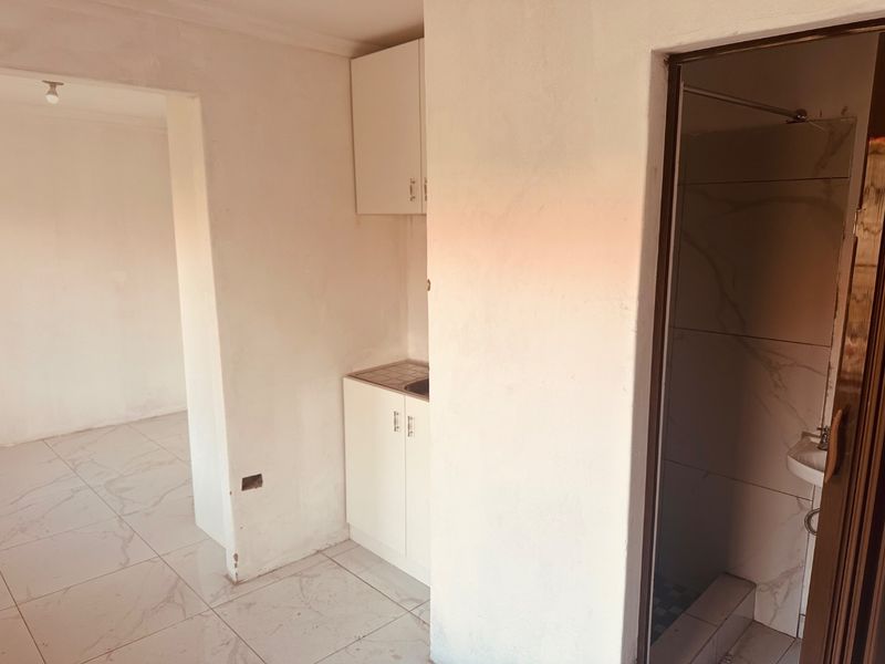 A compact kitchen area featuring built-in cabinetry and sink, adjacent to a tiled bathroom space in an unfinished apartment interior.