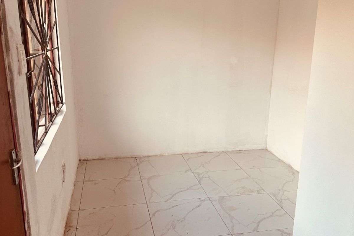 An empty bedroom featuring light-colored marble-effect floor tiles, a window with security bars, and a simple ceiling light fixture.