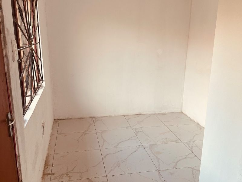 An empty bedroom featuring light-colored marble-effect floor tiles, a window with security bars, and a simple ceiling light fixture.