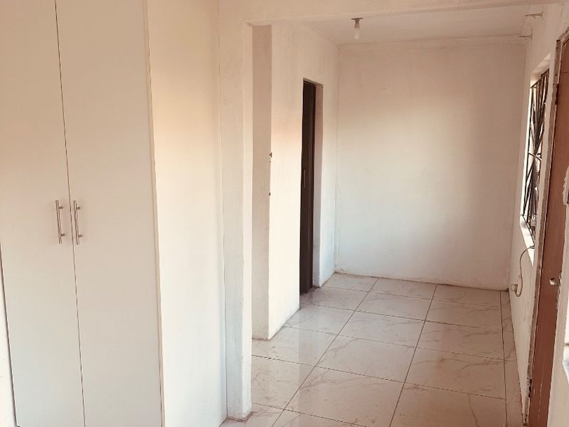 An empty bedroom featuring tiled flooring, a built-in wardrobe, and a security gate on the window.