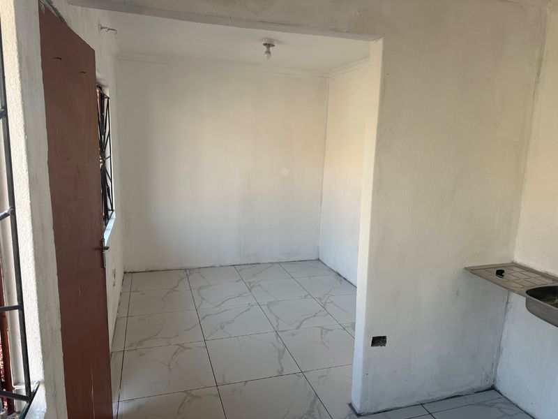 A compact, empty kitchen area featuring tiled flooring, a stainless steel sink, and security bars on the window, awaiting final finishes.
