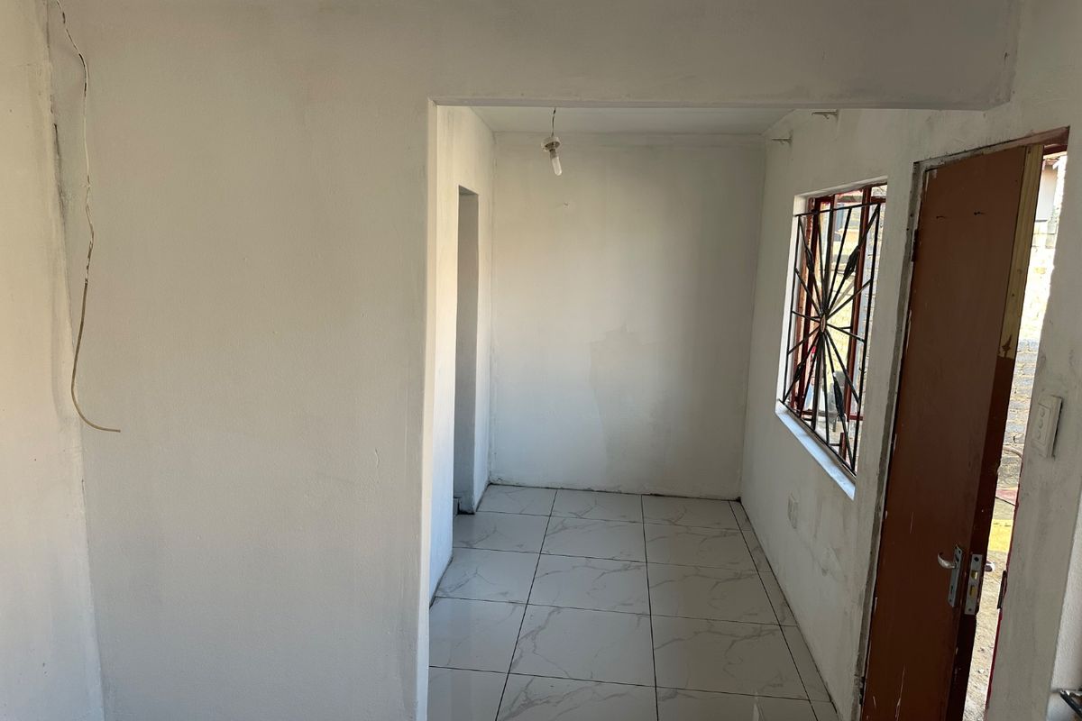 An empty, unfinished living area featuring white walls, tiled flooring, and a window with security bars, requiring final touches and electrical completion.