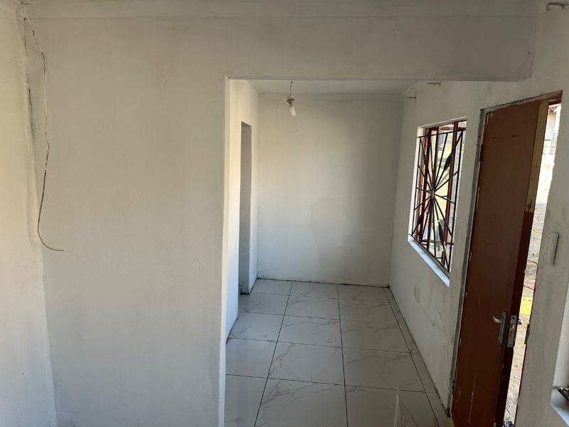 An empty, unfinished living area featuring white walls, tiled flooring, and a window with security bars, requiring final touches and electrical completion.