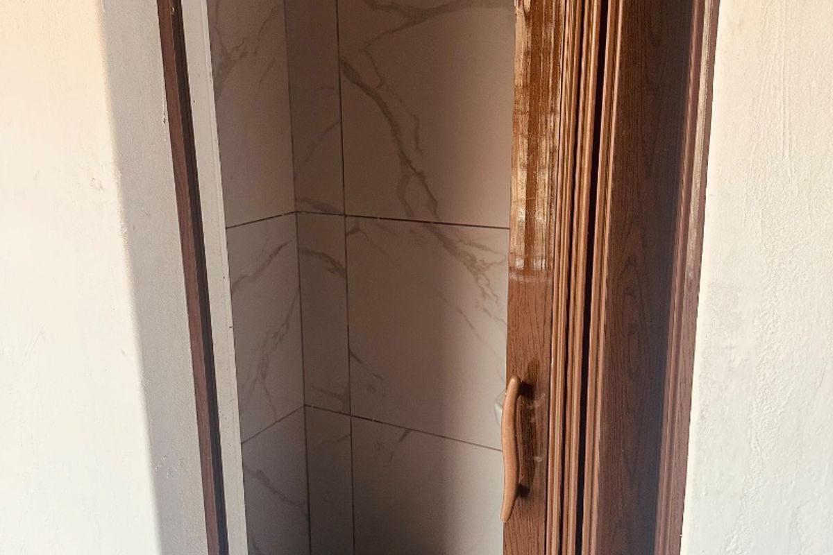A compact shower enclosure featuring marble-look wall tiles, a shower head, and a folding door, requiring some maintenance and cleaning.