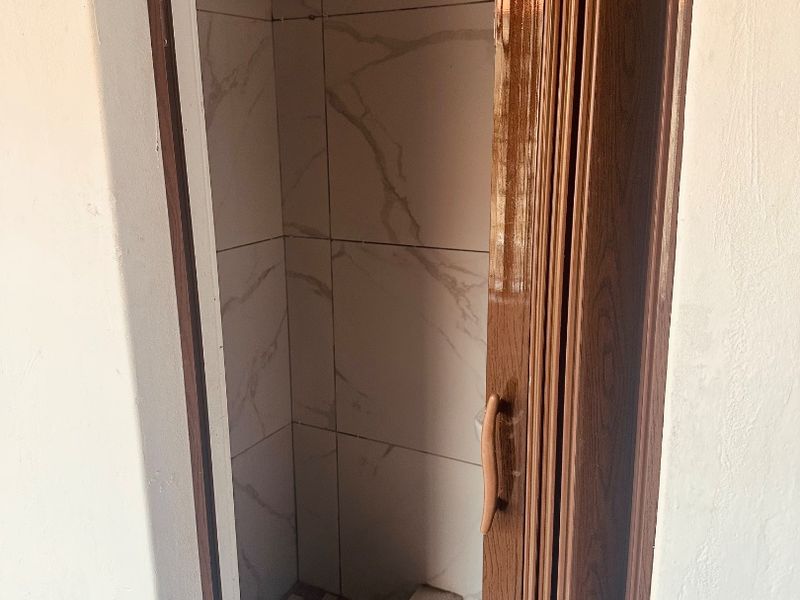A compact shower enclosure featuring marble-look wall tiles, a shower head, and a folding door, requiring some maintenance and cleaning.