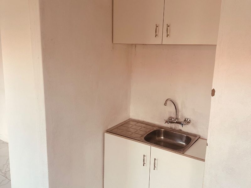 A compact scullery or kitchenette area featuring basic built-in cabinetry, a stainless steel sink, and tiled flooring, currently in need of finishing touches.